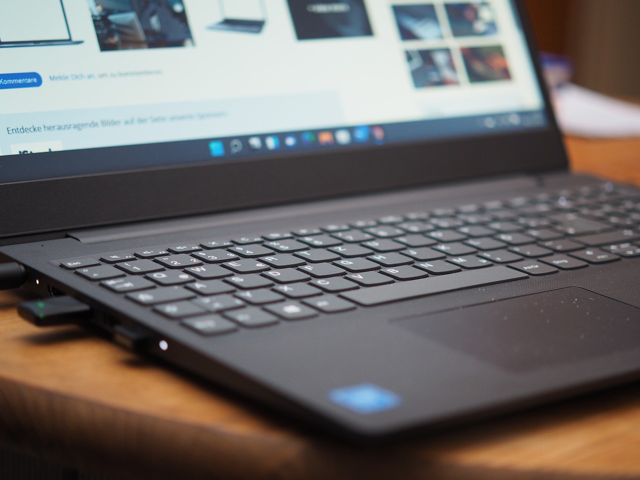Imatge d'un portàtil desplegat, vista des de l'angle esquerre, el portàtil es gris i té una pàgina web oberta, no es pot apreciar del tot la pantalla peró es pot veure que te sistema operatiu windows 11 i un parell de pendrives
